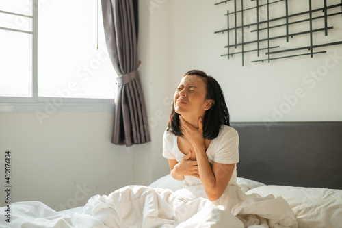 Morning sickness. Young pregnant woman sitting on bed, covering her mouth feeling nauseous during pregnancy, Woman in white pajamas suffering from Acid reflux while wake up on her bed in the morning. photo