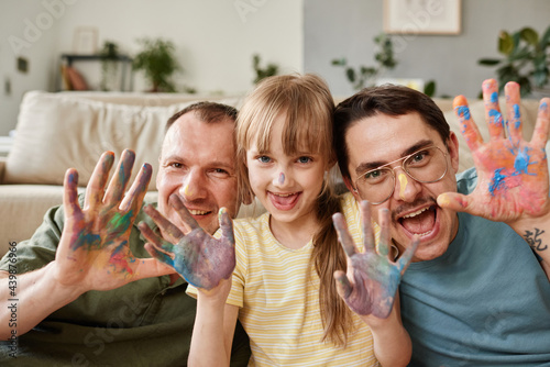 Portrait of happy gay family with child showing their painted hands and smiling at camera photo