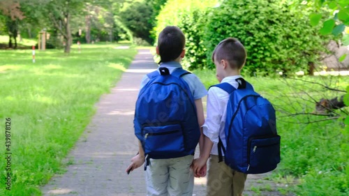 two boys, ,primary school students, children with blue school bags together go to school, holding hands, past houses and green summer trees, Back to school concepttwo boys, ,primary school students photo