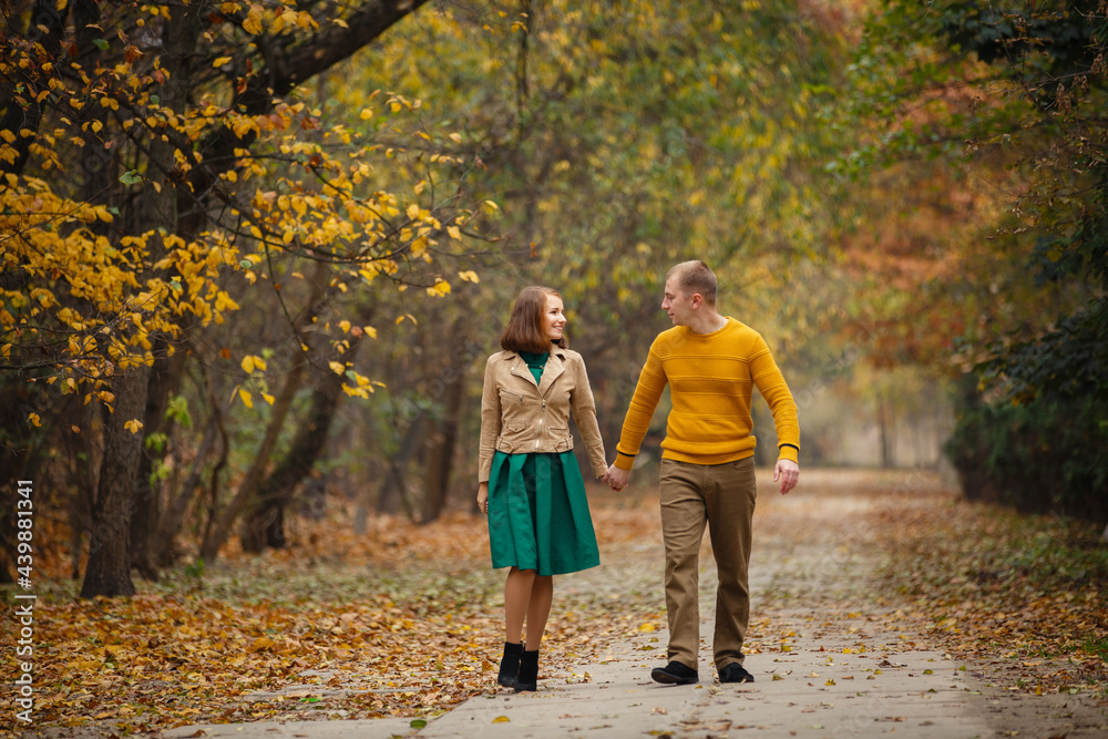Fototapeta premium Happy couple on autumn walk outdoors. Two lovers in autumn park. Love and tender touch. Gentle hugs. Young man and woman in classic autumn colors outfit on a romantic date in a cozy park