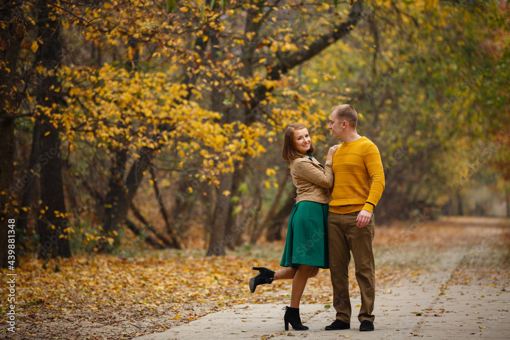 Fototapeta premium Happy couple on autumn walk outdoors. Two lovers in autumn park. Love and tender touch. Gentle hugs. Young man and woman in classic autumn colors outfit on a romantic date in a cozy park