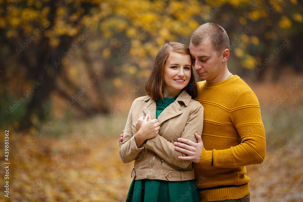 Fototapeta premium Happy couple on autumn walk outdoors. Two lovers in autumn park. Love and tender touch. Gentle hugs. Young man and woman in classic autumn colors outfit on a romantic date in a cozy park