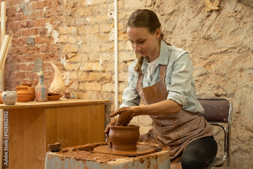 Female potter sculpts a clay pot. The sculptor works with clay on a potter's wheel and at a table