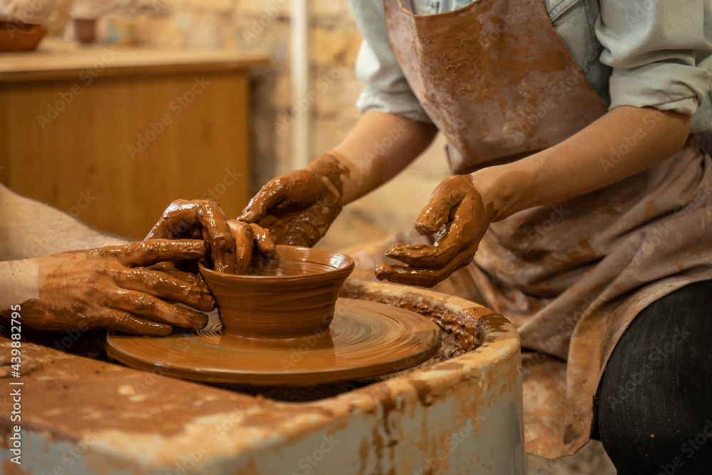 Pottery training, a close-up of a man potter teaches a man how to properly mold a bowl of brown clay on a potter
