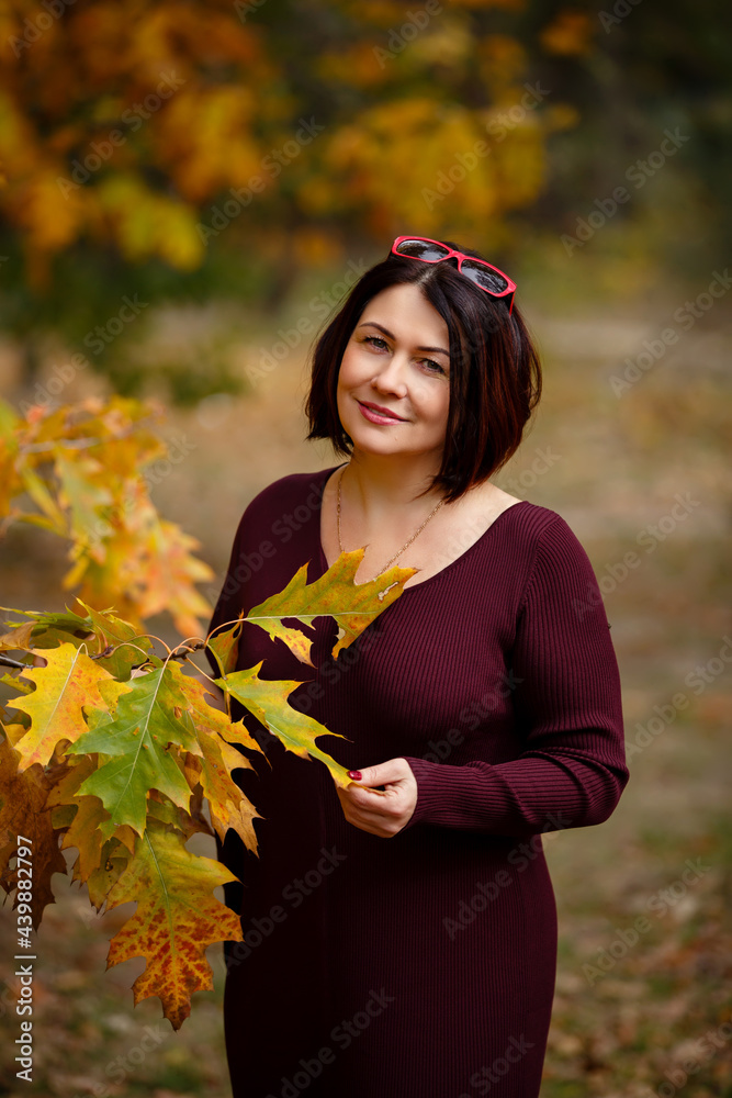 Autumn mood. Beautiful middle-aged woman weared in burgundy color dress is smiling and walking in a park on background of beautiful autumn leaves. Fall coming. Autumn story. Yellow leaves in park. Autumn mood. Beautiful middle-aged woman weared in burgundy color dress is smiling and walking in a park on background of beautiful autumn leaves. Fall coming. Autumn story. Yellow leaves in park.