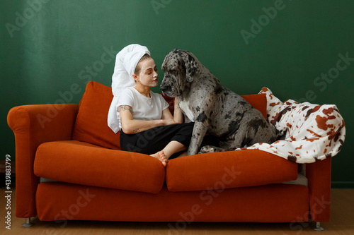 Young woman with cosmetic mask caressing dog on couch photo