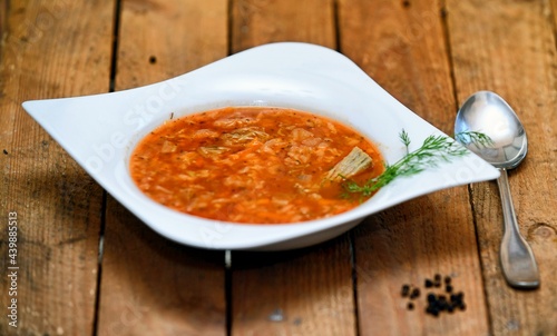 Red tomato soup with pork meat and cabbage in white plate on wooden background. photo