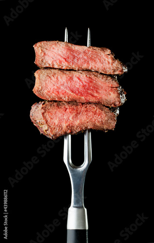 grilled and sliced steak on fork on black background
