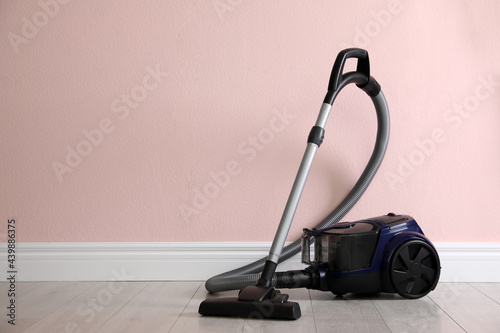 Modern vacuum cleaner near pink wall indoors, space for text