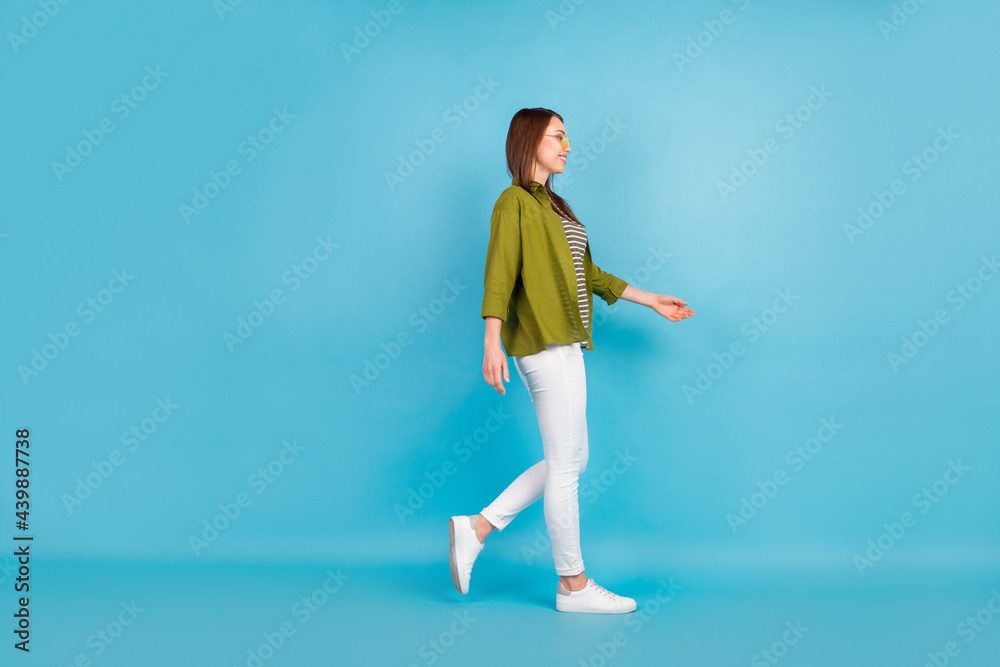 Full size profile side photo young happy positive lady walk empty space smile isolated on blue color background Full size profile side photo young happy positive lady walk empty space smile isolated on blue color background