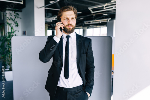 Stylish businessman with a beard in a classic suit is negotiating with partners by phone in a modern office building Business. Social Networking.