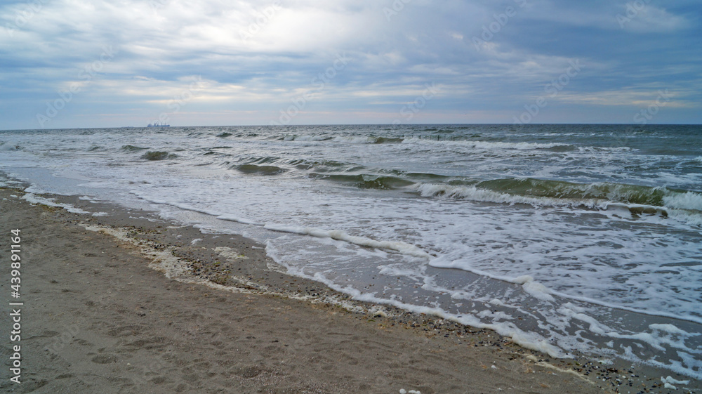Black sea with waves and white foam under the blue sky in the clouds on a spring cloudy day