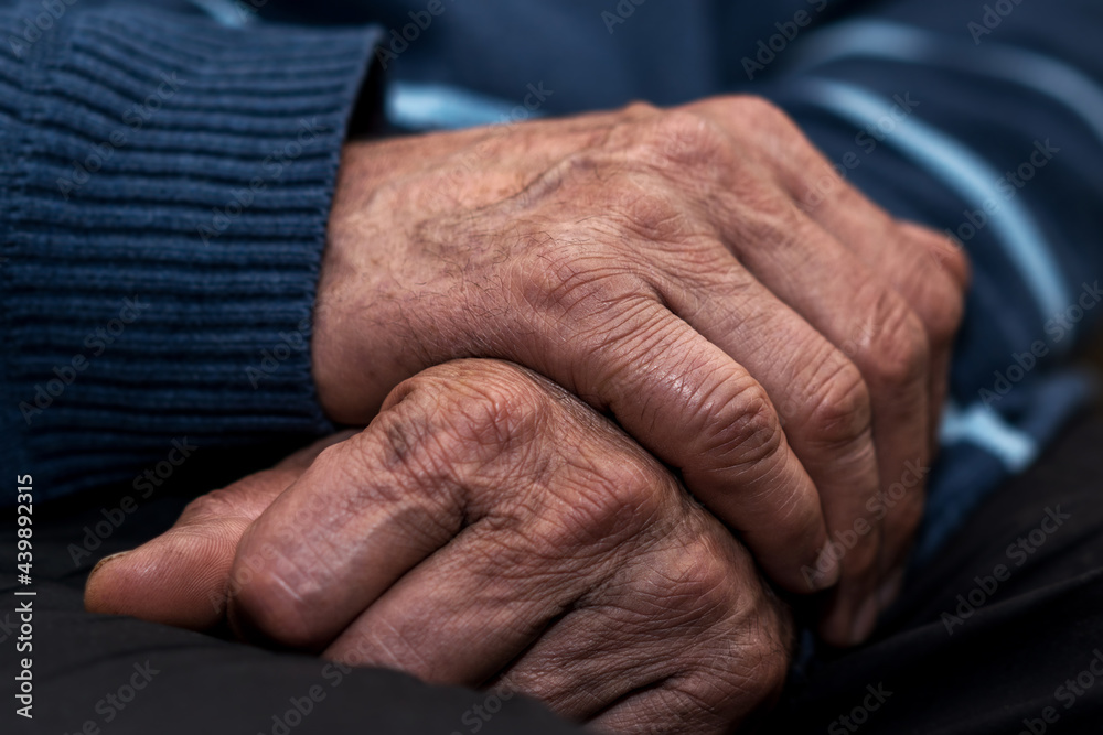 Fototapeta premium Old man holds interlocked wrinkled hands on lap.