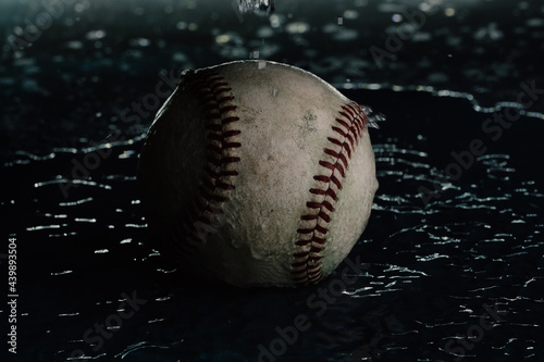 Dark moody baseball in water with shallow depth of field and selective focus close up, sports rain out concept.