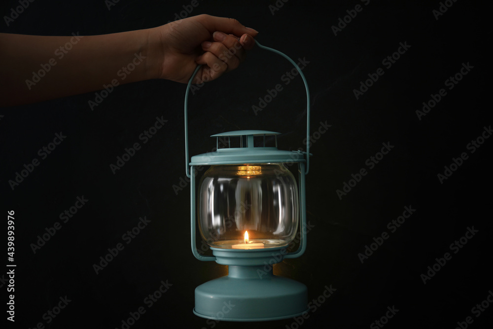 Woman holding lantern with burning candle on black background, closeup