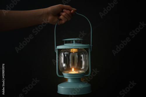 Woman holding lantern with burning candle on black background, closeup