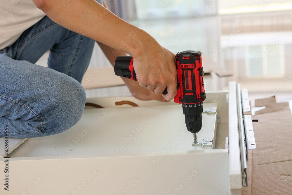 man assembling white table furniture at home using cordless screwdriver
