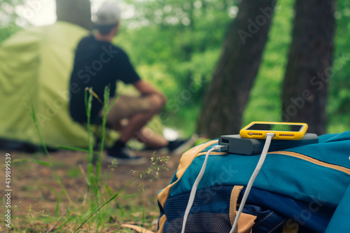Smartphone is charged using a portable charger. Power Bank charges the phone outdoors with a backpack against the backdrop of a tent and a tourist.