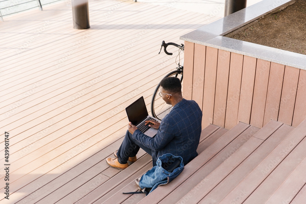 © Mihajlo Ckovric/Stocksy - Young businessman using a laptop outdoors