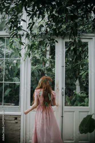 Woman in long dress standing near doorway of glasshouse