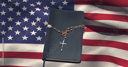 Cross rosary over bible against waving american flag in background