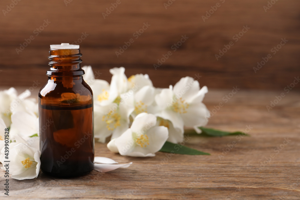 Jasmine essential oil and fresh flowers on wooden table, space for text Jasmine essential oil and fresh flowers on wooden table, space for text