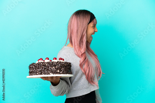 Young woman with pink hair holding birthday cake isolated on blue background laughing in lateral position