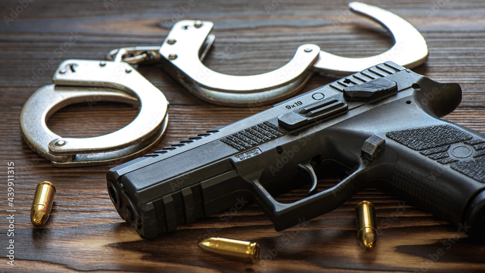 Obraz premium Semi automatic pistol with amunitions and handcuffs on wooden table.