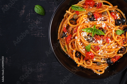 Spaghetti alla puttanesca - italian pasta dish with tomatoes, black olives, capers, anchovies and basil. Top view, flat lay
