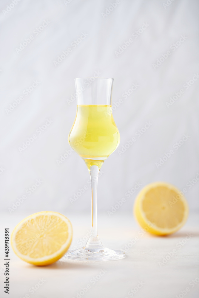 Limoncello in glass, sweet Italian lemon liqueur, traditional strong alcoholic drink and lemons on the blue background.