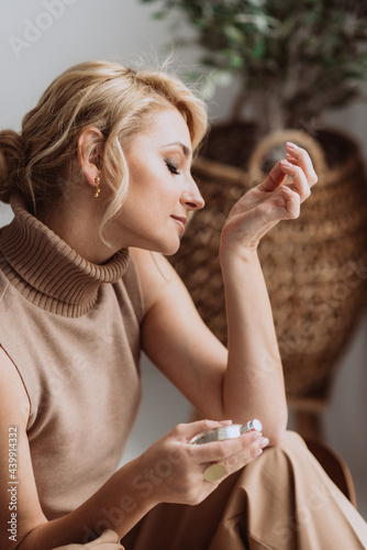 Young beautiful woman holds a bottle of perfume in her hands and inhales while enjoying the fragrance from her wrist. Soft selective focus. photo