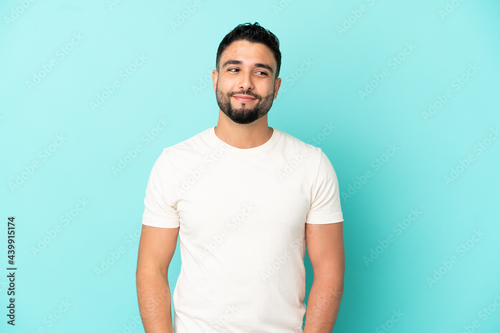 Young arab man isolated on blue background having doubts while looking side