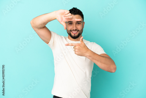 Young arab man isolated on blue background focusing face. Framing symbol