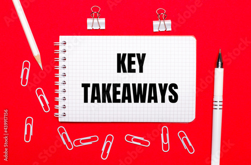 On a red background, a white pen, white paper clips, a white pencil and a notebook with the text KEY TAKEAWAYS. View from above