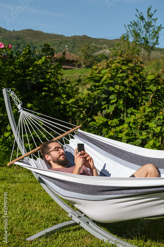Man looking at mobile phone lying in hammock in a rural environment.