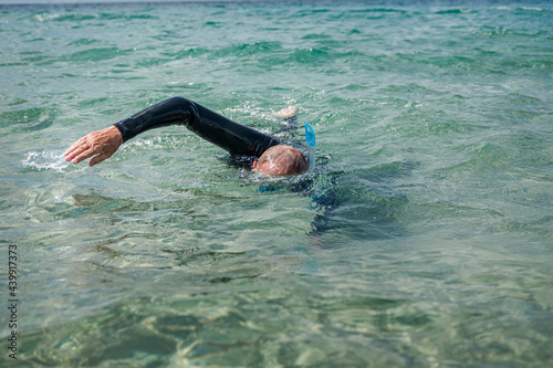 Man in a wetsuit and snorkeling goggles swimming in the sea.