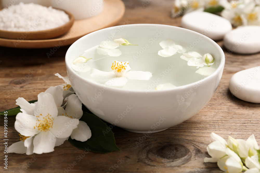 Bowl with water and beautiful jasmine flowers on wooden table