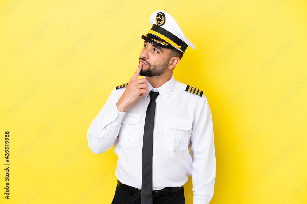 Airplane arab pilot man isolated on yellow background having doubts while looking up