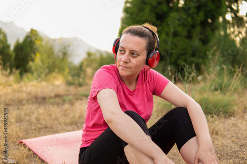 Mujer madura caucasica con auriculares sentada en una colchoneta haciendo ejercicio fisico en el parque