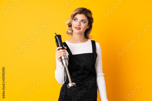 Girl using hand blender isolated on yellow background and looking up