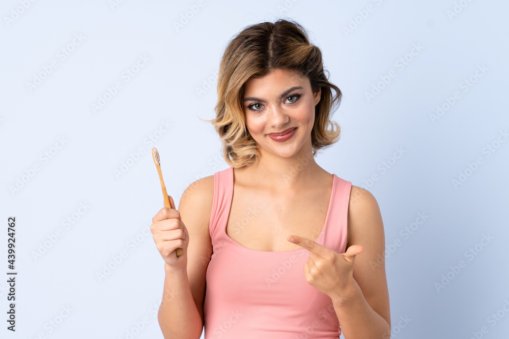 Teenager girl brushing her teeth isolated on blue background and pointing it Teenager girl brushing her teeth isolated on blue background and pointing it