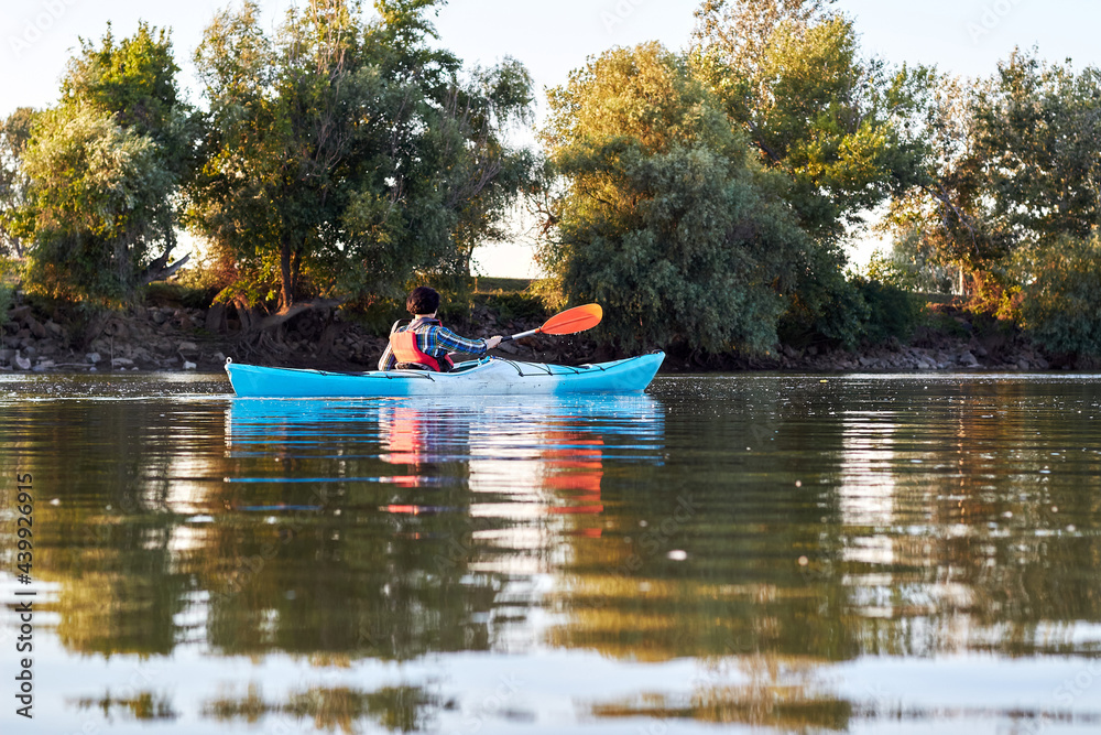 Woman kayaking on blue kayak in summer Danube river near trees