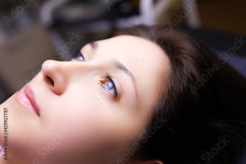 a model girl with blue eyes is lying on a permanent makeup procedure her eyebrows are being prepared for powder spraying