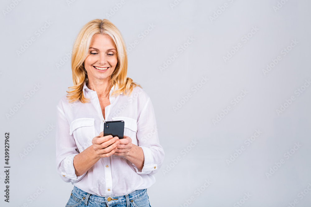 Happy mature senior woman holding smartphone using mobile online apps, smiling old middle aged lady texting sms message chatting on phone looking at cellphone isolated on white grey background Happy mature senior woman holding smartphone using mobile online apps, smiling old middle aged lady texting sms message chatting on phone looking at cellphone isolated on white grey background