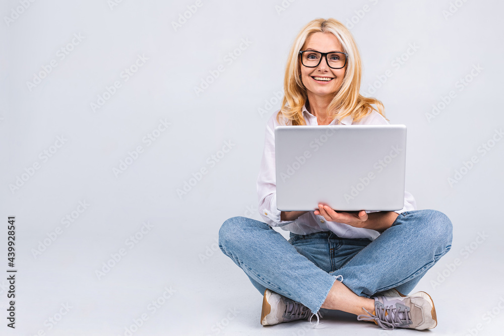 Naklejka premium Business concept. Portrait of happy senior aged woman in casual sitting on floor in lotus position and holding laptop isolated on white background. Copy space for text.