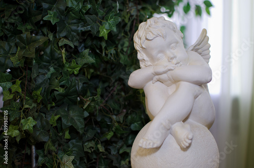 sculpture of a sleeping angel made of white stone on a background of green leaves. Valentine's Day.