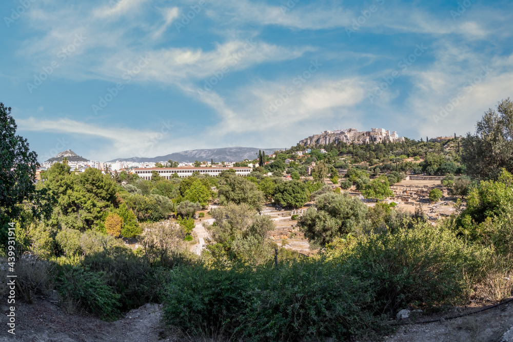 Ancient Agora of Athens archaeological site panoramic view. Stoa of Attalus (left), Acropolis rock (right) in the background. Athens, Attica, Greece. Sunny day, cloudy blue sky