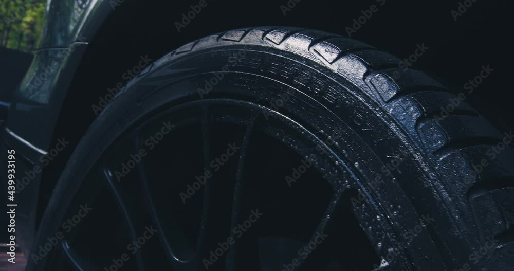 Close up of washing wheel tyre with spraying soapy water in car wash. Exterior car detailing concept