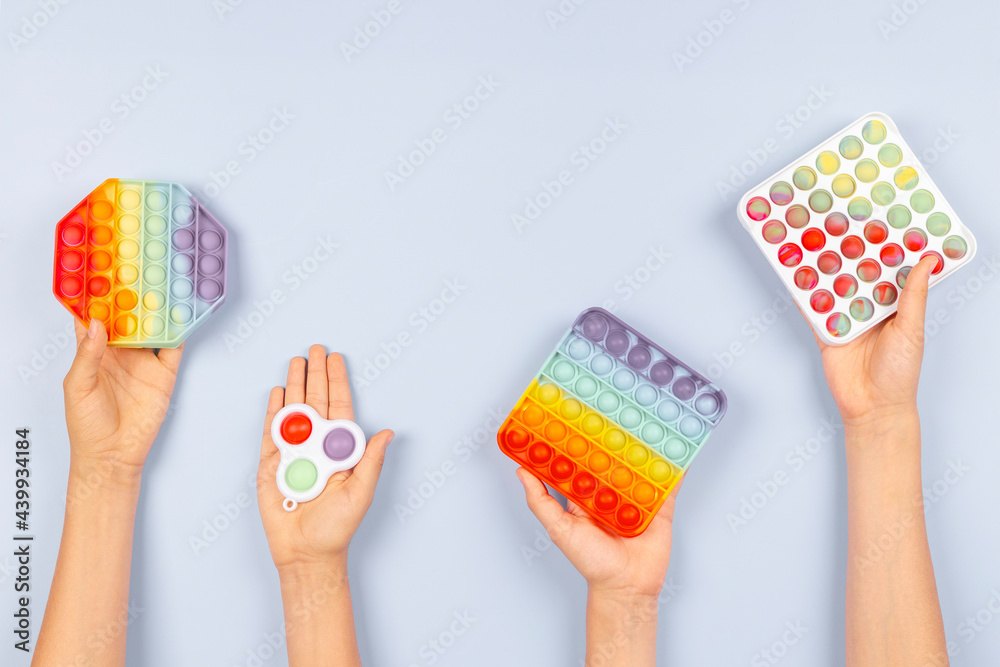 Many hands holding colorful pop it fidget toys on blue background. Push pop-it fidgeting game helps relieve stress, anxiety, autism, provide sensory and tactile experience for children Many hands holding colorful pop it fidget toys on blue background. Push pop-it fidgeting game helps relieve stress, anxiety, autism, provide sensory and tactile experience for children