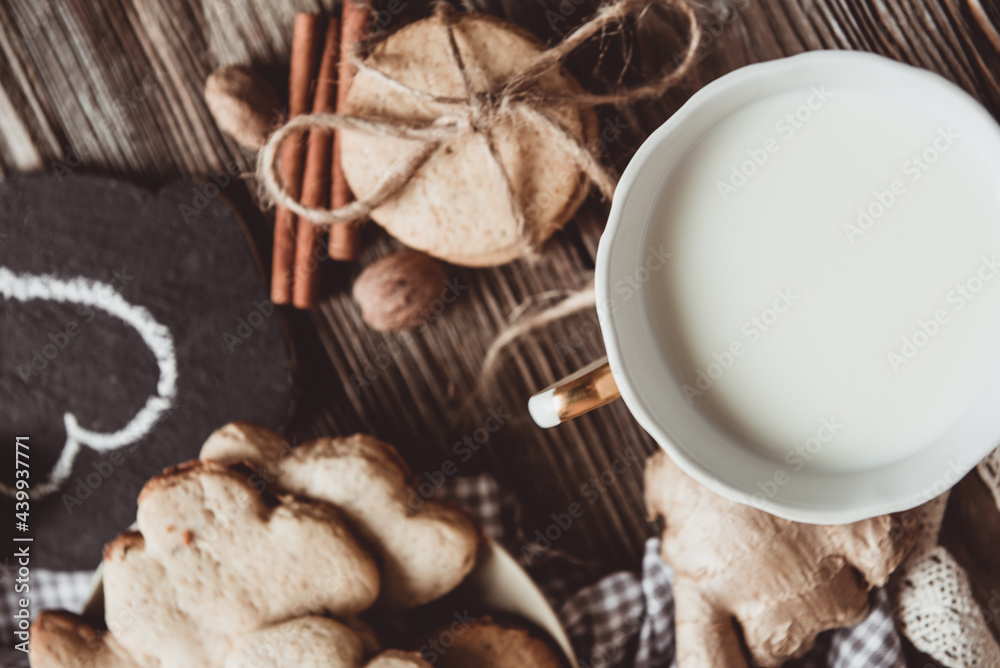 Close up of homemade ginger cookies, cinnamon, ginger with cup of milk on a towel wooden table. Copy space. Retro toned image, flat lay Close up of homemade ginger cookies, cinnamon, ginger with cup of milk on a towel wooden table. Copy space. Retro toned image, flat lay